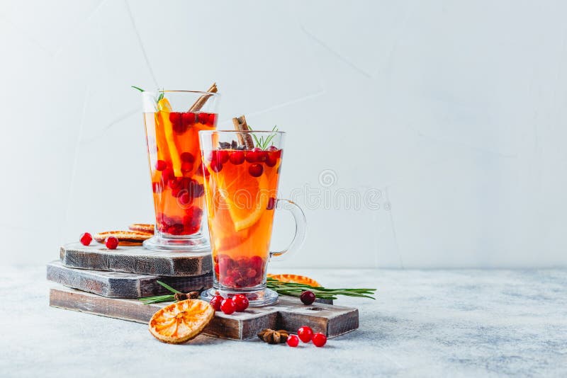 Orange and cranberry drinks with orange slices and spices. Hot drinks for winter and Christmas, Hot tea with orange slices, cranberries and rosemary in tall glasses. Hot drinks for winter and Christmas. Place for text