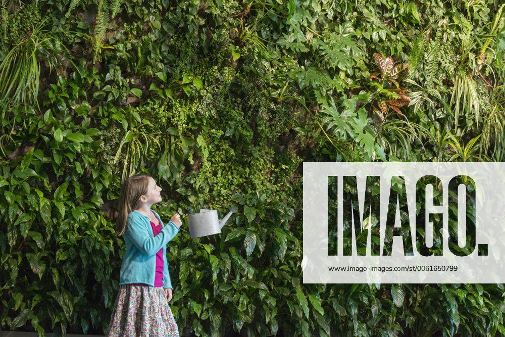IMAGO Creative: Nächste Generation, Sozial- und klimabewusst Outdoors in the city in spring. An urban lifestyle. A young girl standing in front of a wall covered with ferns and climbing plants.