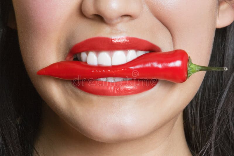 Close-up portrait of Hispanic woman biting red pepper, Close-up portrait of Hispanic woman biting red pepper model released