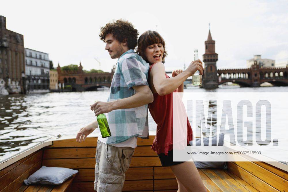 Germany, Berlin, Young couple on motorboat, holding bottles, standing back to back model released property released VVF00052