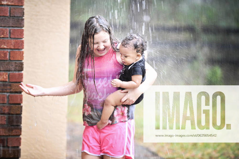 Girl and baby playing in rain, both smiling and enjoying. United States, Florida, Inverness R_YWQX240623D-1468461-01 ,model released, Symbolfoto