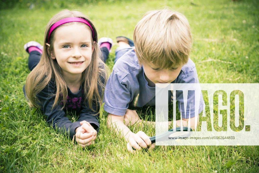 Brother and sister lying on meadow watching flowers with magnifying glass model released SARF000673