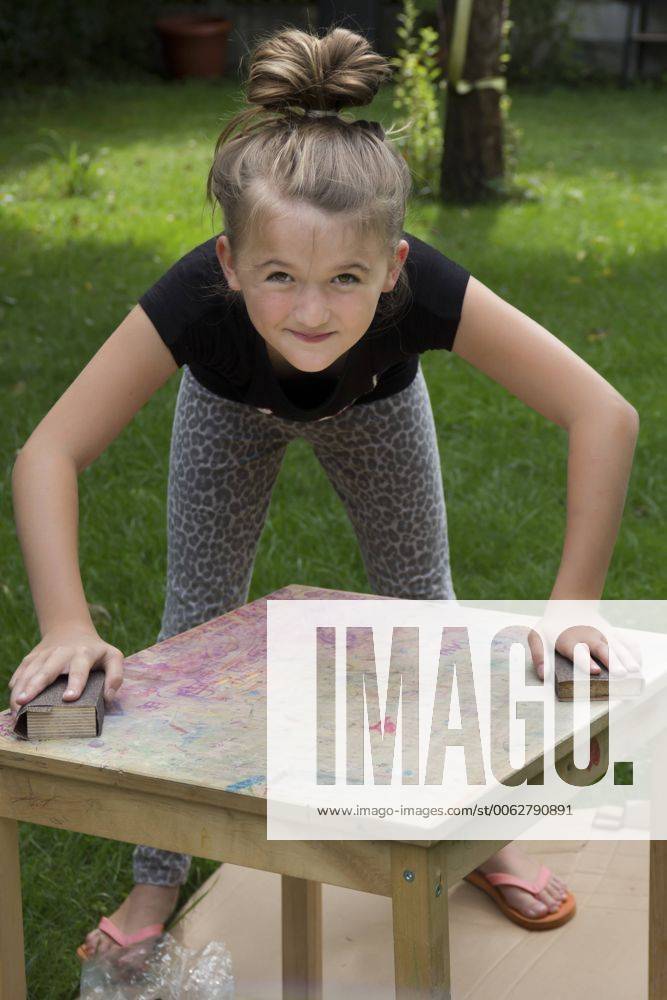 Girl standing in the garden working on a wooden table with sandpaper blocks model released Symbolfoto YFF000223