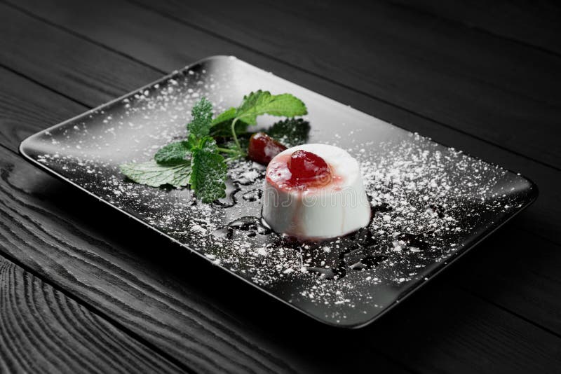 Photo of italian panna cotta dessert with strawberry sirup and mint leaf on the black wooden background., Photo of italian panna cotta dessert with strawberry sirup and mint leaf on the black wooden background