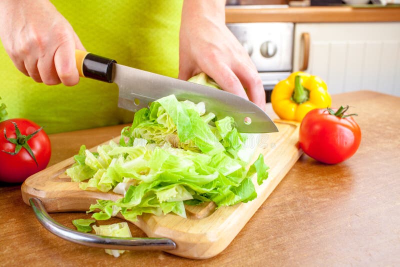 Woman`s hands cutting vegetables, Woman`s hands cutting lettuce, behind fresh vegetables.