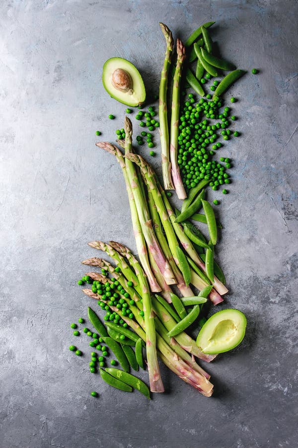 Young Green asparagus, Variety of raw uncooked organic young green vegetables asparagus, peas, pod pea, avocado over grey texture background. Top view, copy space. Healthy eating