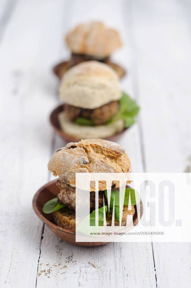 Three garnished bread rolls with patty and lamb s lettuce on wood ODF000886
