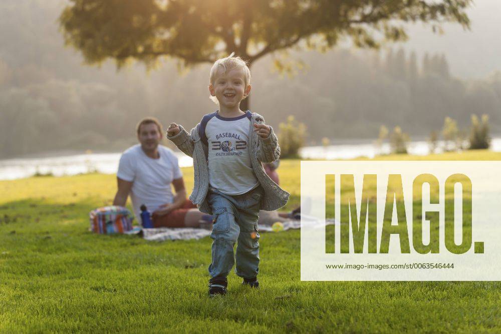 Happy boy running on meadow with family in background model released Symbolfoto PAF001200