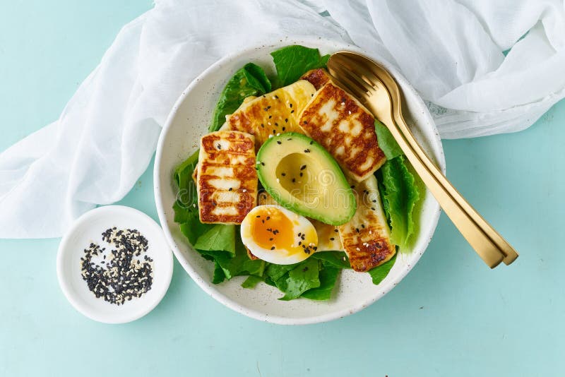 Keto ketogenic diet soft boiled eggs with avocado and lettuce on pastel background top view, Keto ketogenic diet soft boiled eggs with grilled haloumi, avocado and lettuce, mediterranean cuisine on pastel background