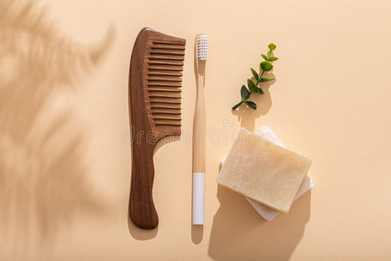 Eco friendly tools, Wooden hair comb, eco bamboo toothbrush, natural soap on beige pastel background with tropical leaves shadows on sunny morning. Washing and tooth cleaning morning routine, zero waste living, top view .
