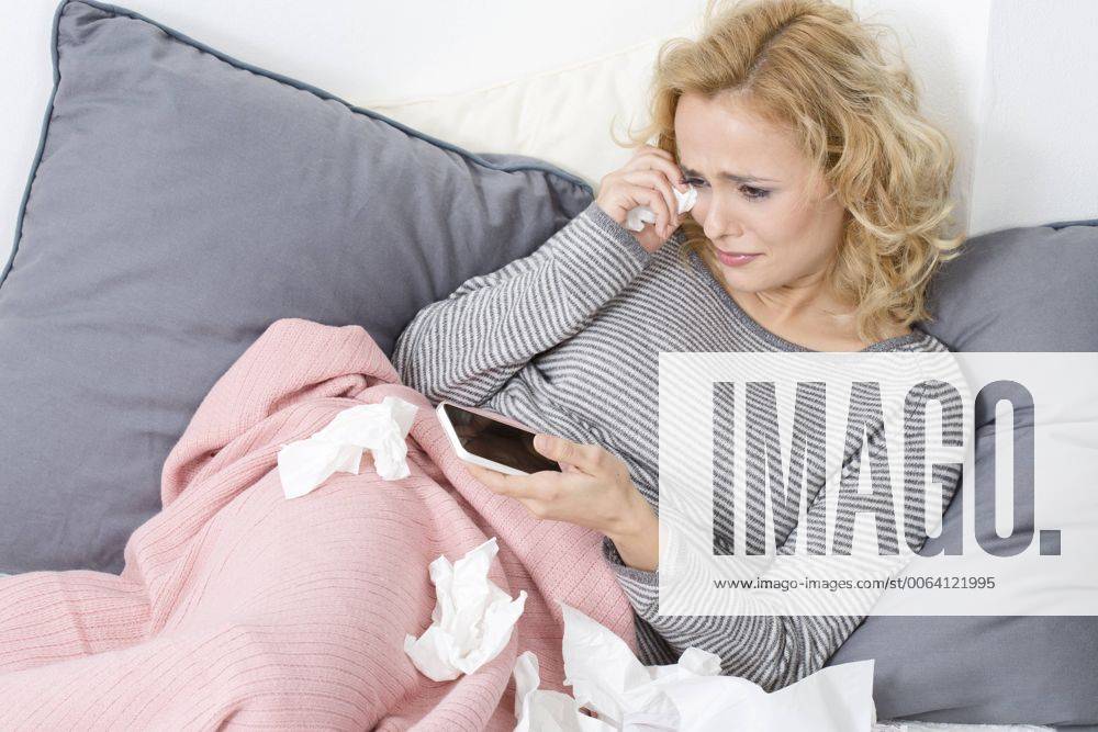 Crying woman lying on couch holding cell phone model released Symbolfoto MAEF009938