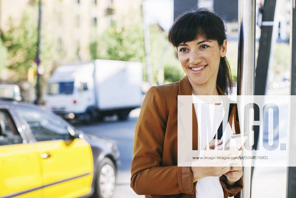Spain, Barcelona, portrait of smiling businesswoman with smartphone waiting at the bus stop model released Symbolfoto EBSF000594