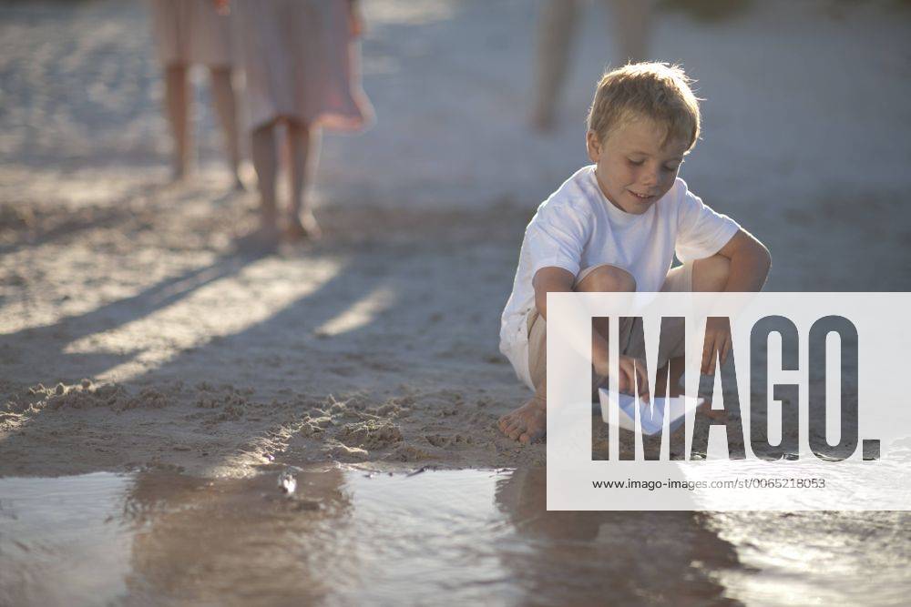 Boy playing with paper boat at a water pool on a sandy beach model released Symbolfoto ZEF004781