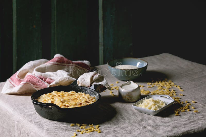 American dish mac and cheese, Classic american dish baked mac and cheese in cast iron pan with kitchen towel and ingredients above on kitchen table with linen tablecloth. Dark rustik style