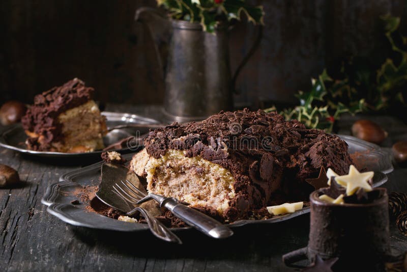 Sliced christmas chocolate yule log, Sliced homemade Christmas chocolate yule log with chestnuts cream on vintage plate with forks, chocolate stars and holly branch over old wooden table. Dark rustic style.
