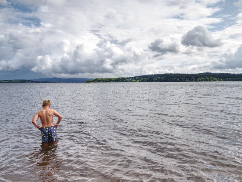Little joyful Caucasian funny boy try cold water of lake, Little joyful Caucasian funny boy try cold water of lake. Kid stay in water with level at knee, vitality, swimming, suit, shorts, pants, swimmer, sunbeam, summertime, splash, son, smile, seashore, scenic, sand, river, rest, poor, pond, play, natural, low, view, angle, lonely, laughing, lad, hot, holiday, hard, happiness, floundering, expression, enthusiasm, dynamic, droplet, cowards, cooling, weather, childhood, cheer model released
