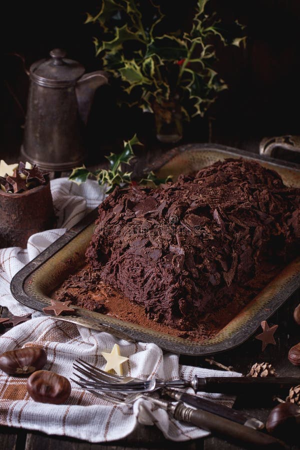 Homemade christmas chocolate yule log, Whole homemade Christmas chocolate yule log with chestnuts cream on vintage tray with white textile rag and chestnuts, chocolate stars and holly branch over old wooden table. Dark rustic style.