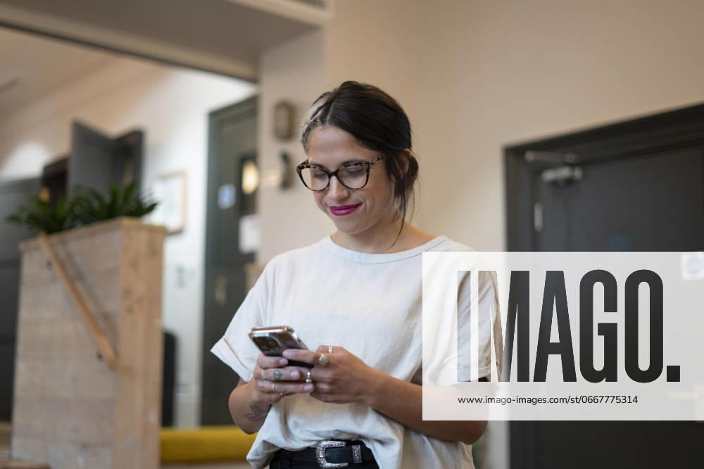 Smiling woman using smart phone in office model released
