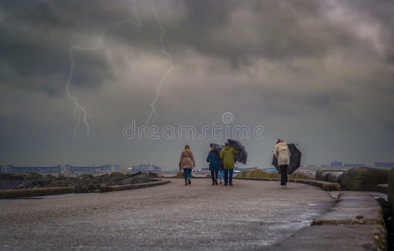 A group of people walking and trying to keep umbrellas in a windy day and lightning in background, A group of people walking and trying to keep umbrellas in a windy day and lightning in background