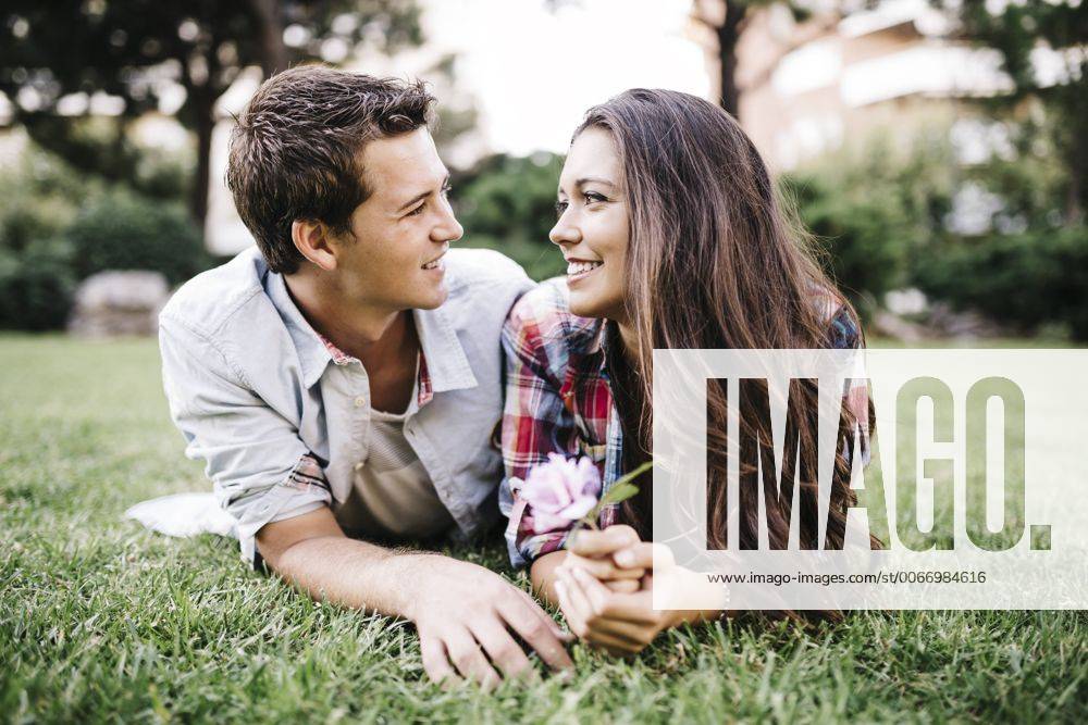 Young couple in love lying on a meadow in a park looking at each other JRFF000109