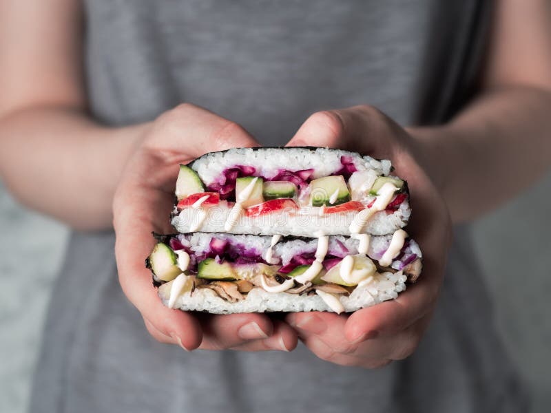 Vegan onigirazu in woman hands, Vegan sushi sandwich onigirazu with mushrooms and vegetables.Healthy dinner recipe and idea. Colorful japan big roll sandwich onigirazu with red cabbage,radish,cucumber,mushrooms.Trend food.Copy space