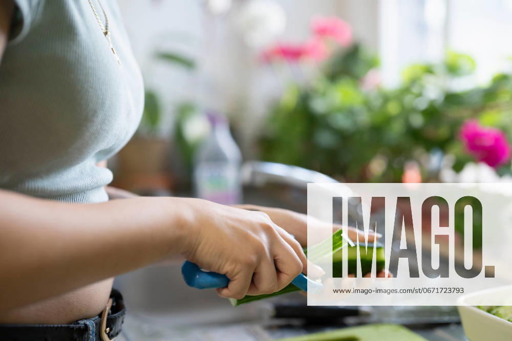 Close-up of young woman peeling vegetables in kitchen model released
