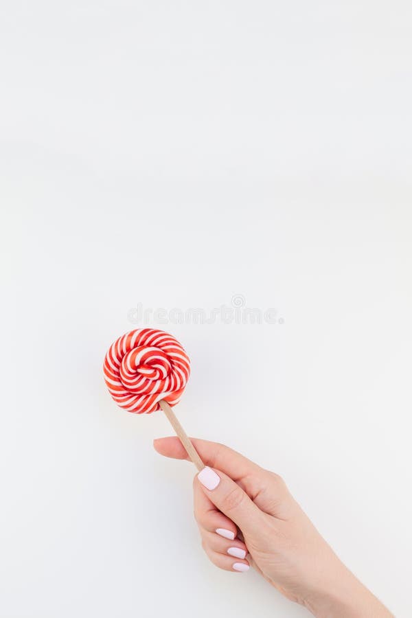 Woman hand with red lollipop, Woman hand with pastel manicure polish holding bright red swirling lollipop isolated on white background copy space minimalism style. Template for feminine social media. Fun and celebration concept