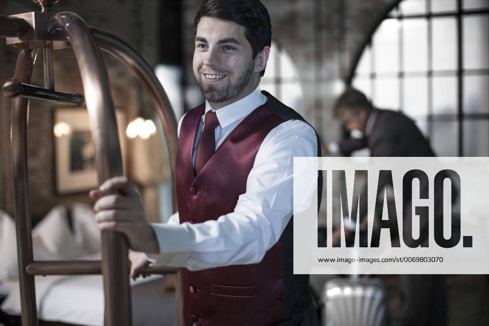 Bellboy with trolley, business man with suitcases in background, hotel room model released Symbolfoto property released ZEF008032