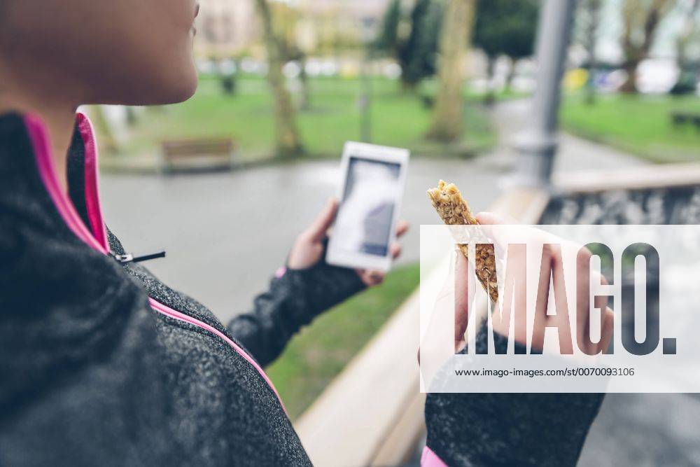 Woman eating cereal bar after training and holding smart phone model released Symbolfoto DAPF000039