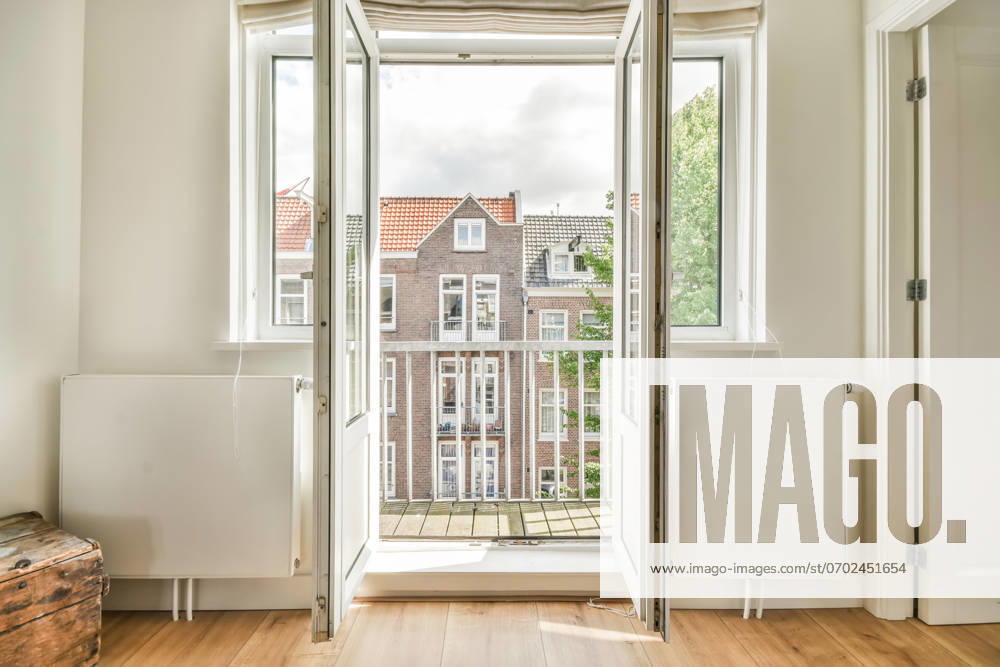 A refreshing interior design featuring an open balcony door leading to a view of traditional city architecture, inviting natural light and air into a clean, modern room. Model Released ProCreators_ID5204_167502_003