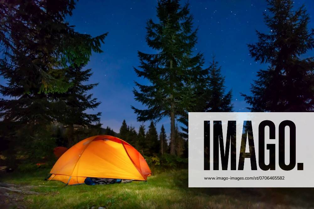 Orange illuminated tent in dark night forest with night sky and stars ,model released, Symbolfoto