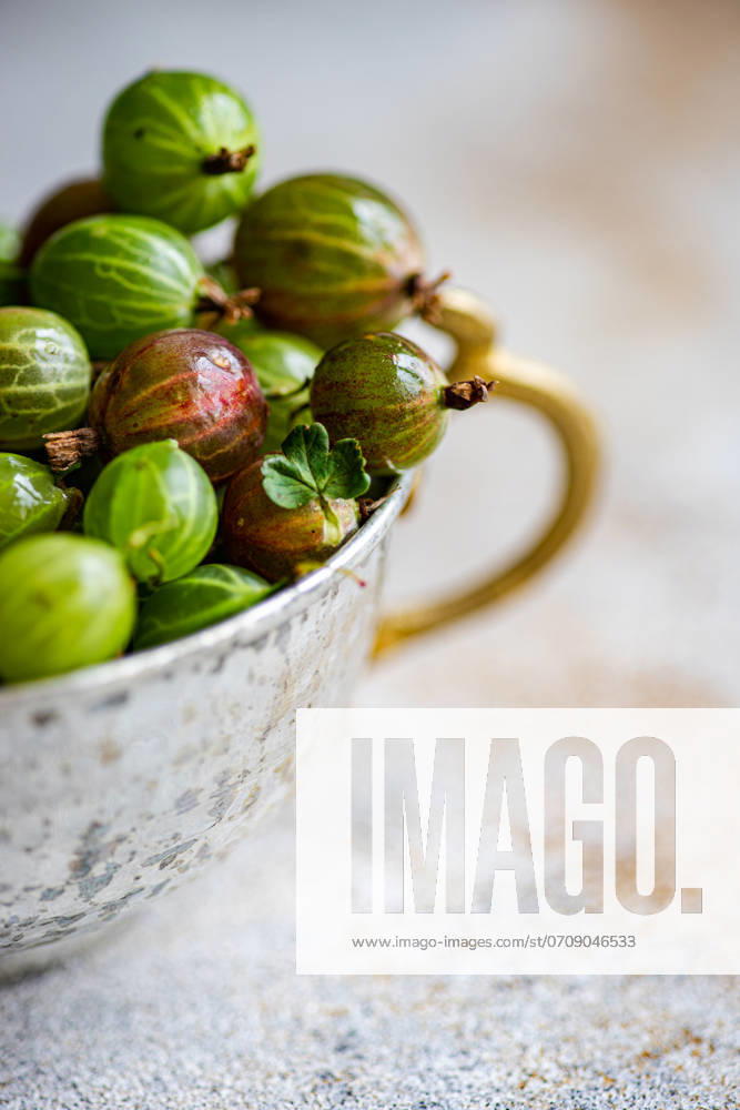 Close-up of fresh organic gooseberries in a rustic, tarnished metal cup set against a soft-focus background. The vibrant green and red tones of the berries highlight their ripeness and natural appeal. Model Released AnnaBogush_ID22657_660675_002