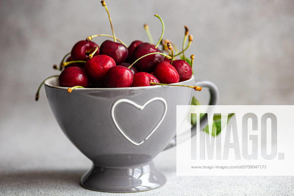 IMAGO Creative, Jahreszeit Sommer, Kirschen Ripe red cherries in a modern grey bowl with a heart-shaped cutout, placed on a textured grey background. The image captures the vibrant color and freshness of the cherries, suitable for culinary and lifestyle themes. Model Released AnnaBogush_ID22658_660688_007