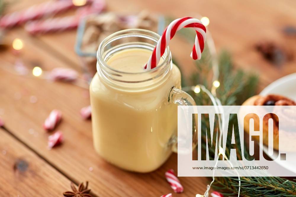 Christmas and seasonal drinks concept - eggnog in glass mug with candy cane decoration, cinnamon buns, fir tree brunch and garland lights on wooden background. eggnog with candy cane in mug and cinnamon buns ,model released, Symbolfoto