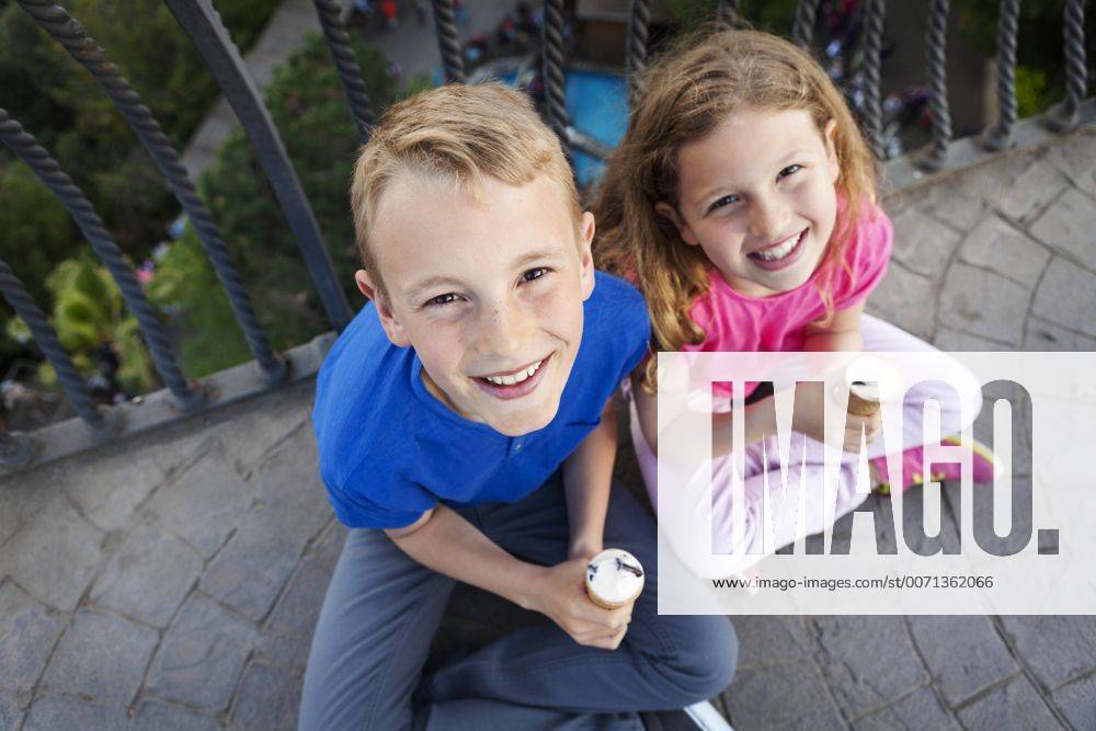 Portrait of brother and sister with ice cream cones sitting on balcony looking up to camera model released Symbolfoto VABF000472