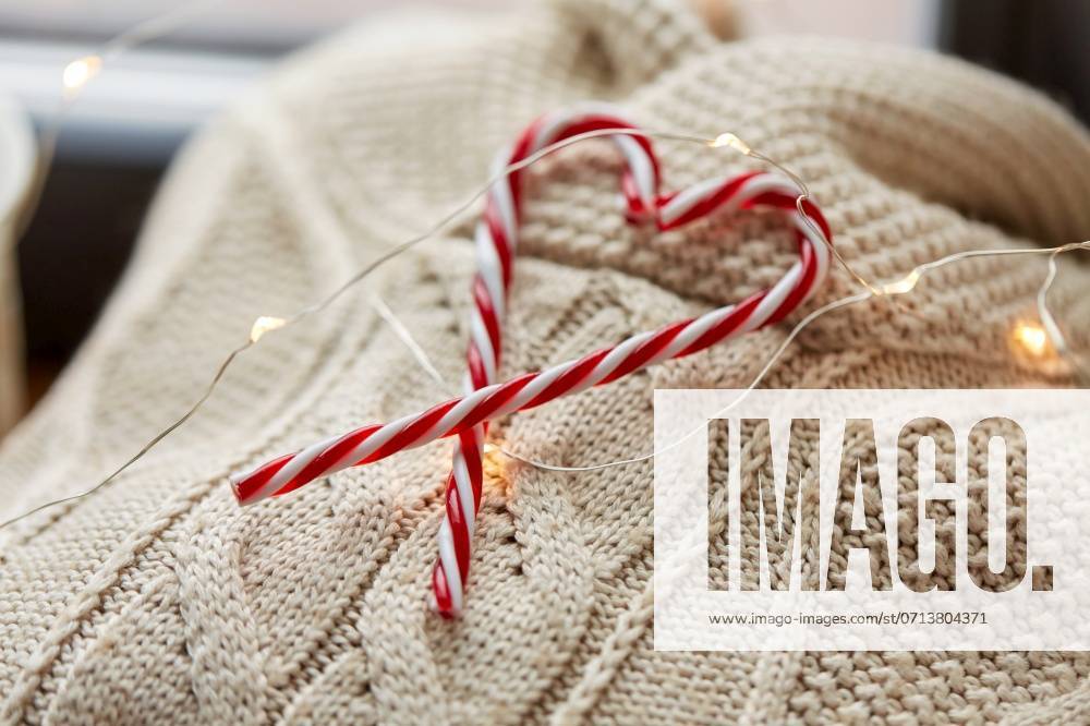 Christmas, clothes and objects concept - close up of warm wool braided sweater, candy cane and electric garland string at home. close up of sweater, candy cane, christmas garland ,model released, Symbolfoto