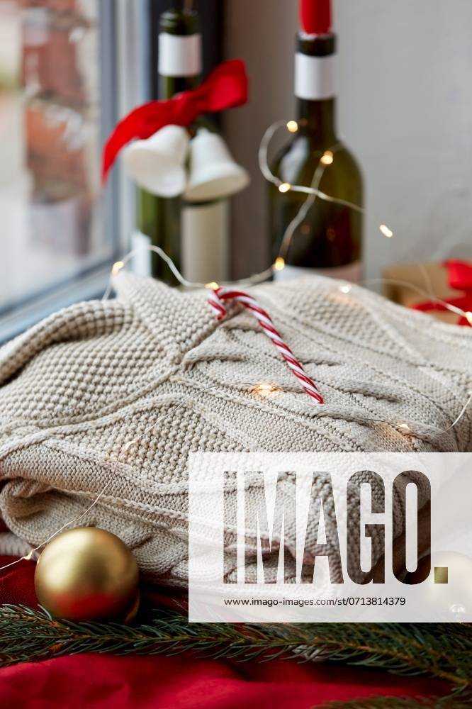 Christmas, clothes and objects concept - close up of warm wool braided sweater, candy cane and electric garland string at home. close up of sweater, candy cane, christmas garland ,model released, Symbolfoto
