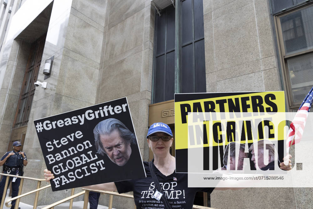 An anti-Trump protester holds an American flag and signs with an image of Steve Bannon that reads GreasyGrifter Steve Bannon GLOBAL FASCIST and a sign with an image of Bannon and Trump together that reads PARTNERS IN CRIME outside of the Manhattan District Attorney s Office while awaiting a court appearance by Bannon (Not Pictured) for his fraud, money laundering and conspiracy case. New York USA - ZUMAr174 20240723_znp_r174_010