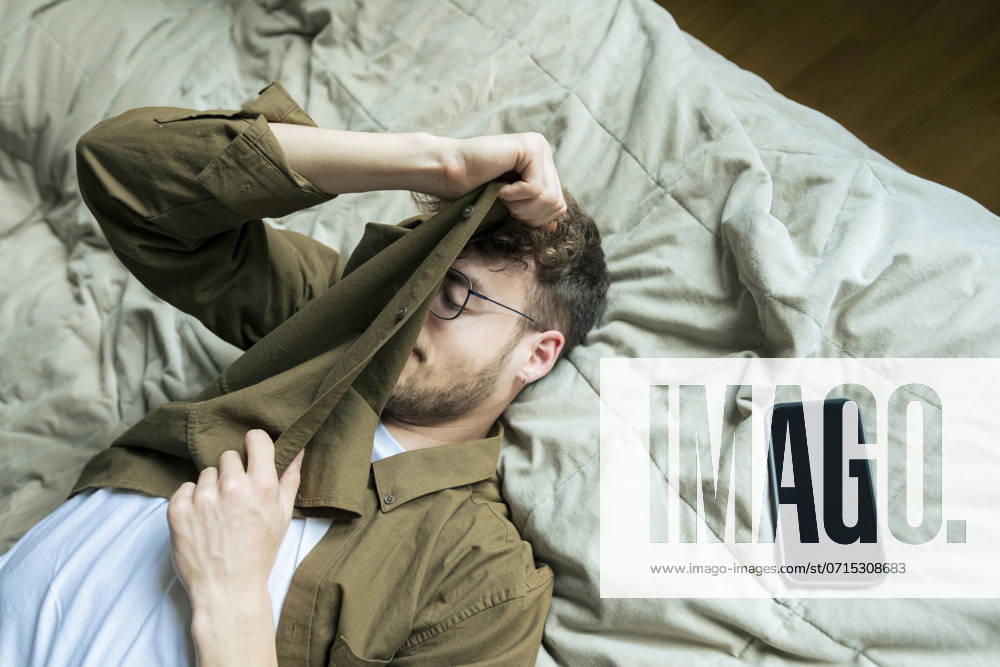 Tired young man lying by smart phone on bed at home model released, Symbolfoto property released, KNSF10356