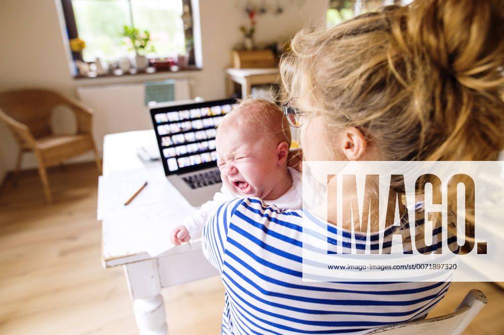 Mother at desk at home holding crying baby model released Symbolfoto property released HAPF000475