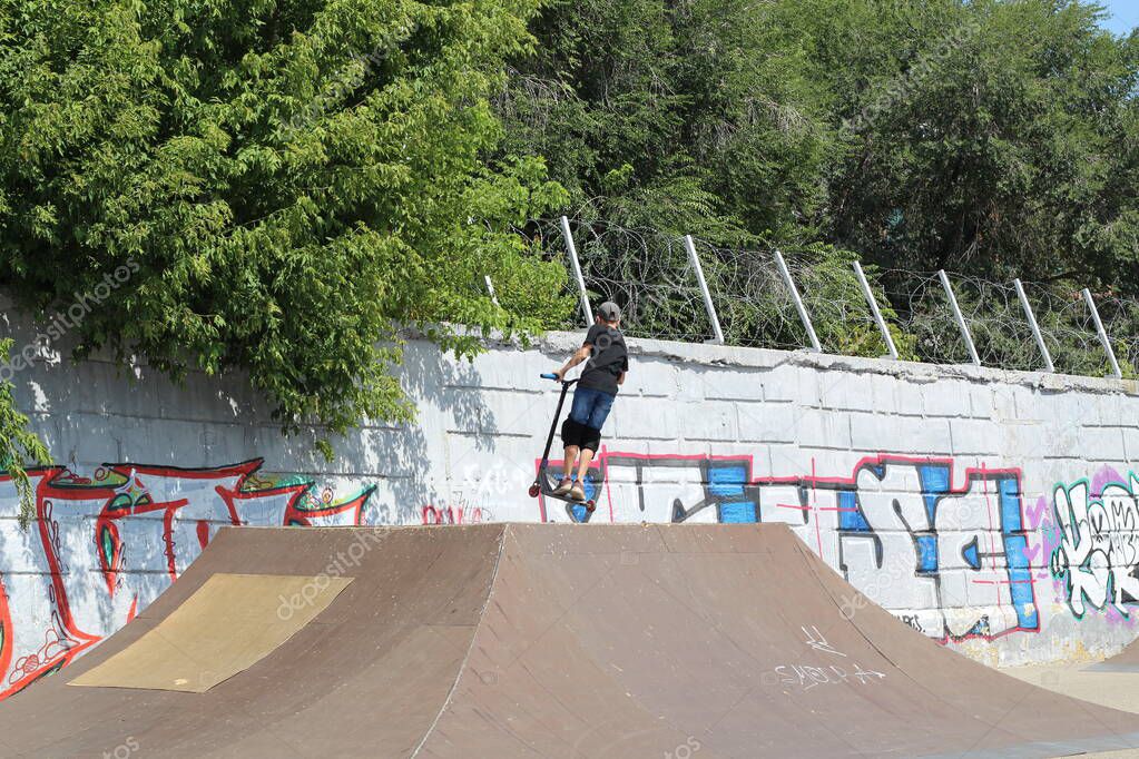 Boy on scooter makes a trick and enjoying his riding by skate in the skate park