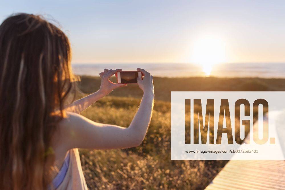 Youniverse - Young Holidays Young woman photographing beach at sunset with smart phone model released Symbolfoto MGOF001999