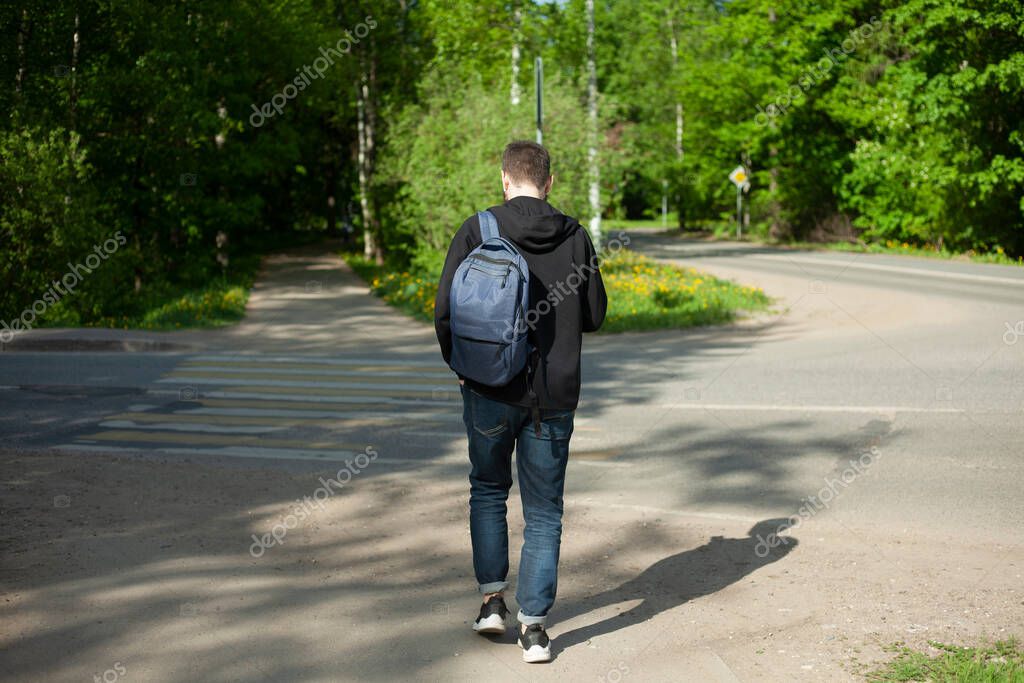 A guy with a backpack walks along the road. The man on the pedestrian road. The man from the back. The man goes to work.