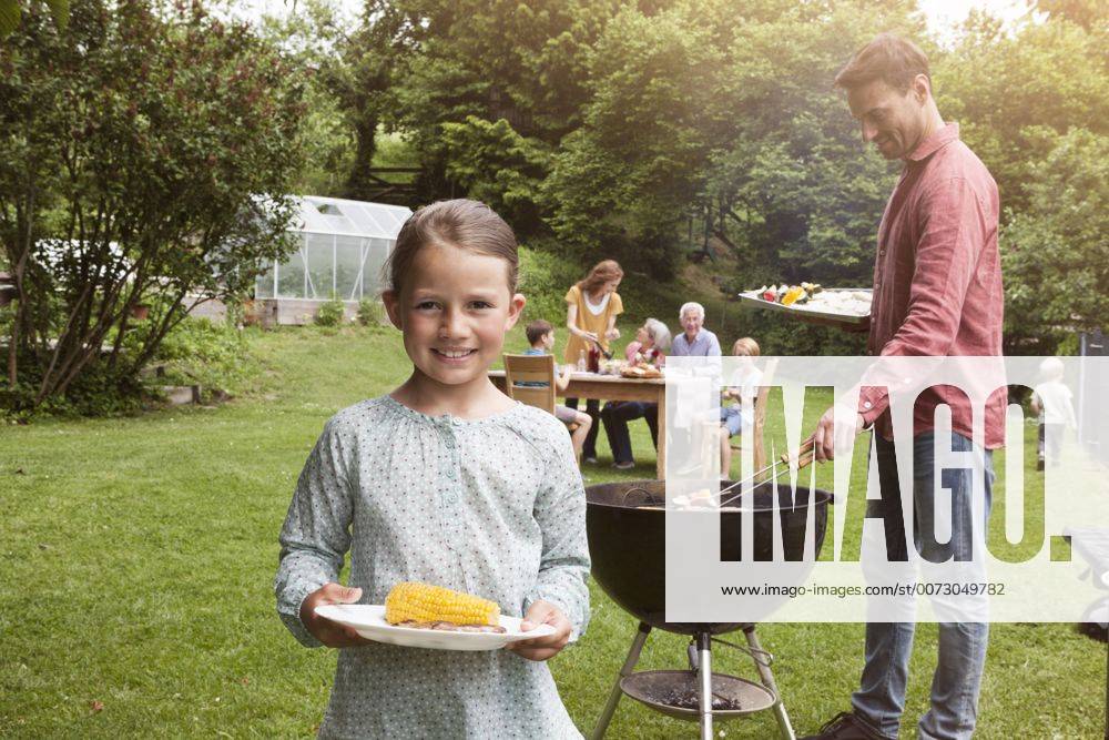 Grillen mit der Familie - Model Released Smiling girl holding plate with corn cob on a family barbecue model released Symbolfoto property released RBF004773