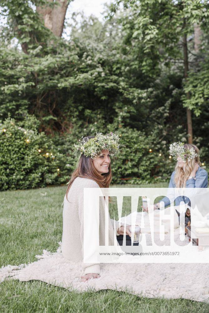 Two smiling women with a flower wreaths in their hair sitting in a garden. Two smiling women with a flower wreaths in their hair sitting in a garden. 22472