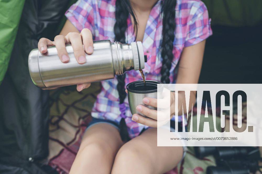 Young woman sitting in a tent pouring coffee from thermos flask into cup, partial view model released Symbolfoto DAPF000261