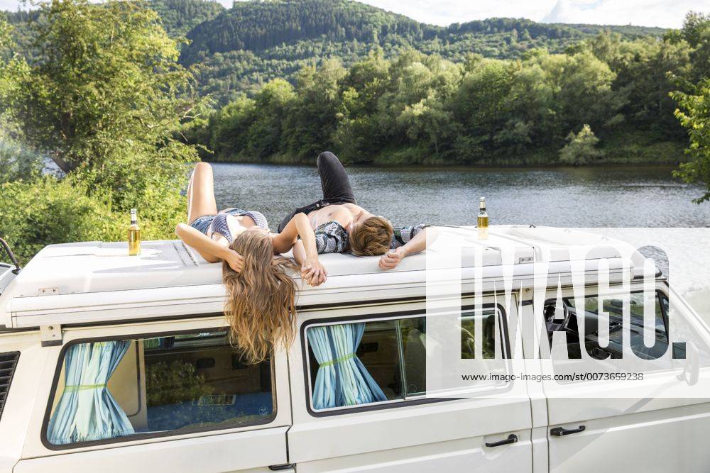 Youniverse - Young Holidays Young couple lying on roof of a van at lakeside model released Symbolfoto property released FMKF002862