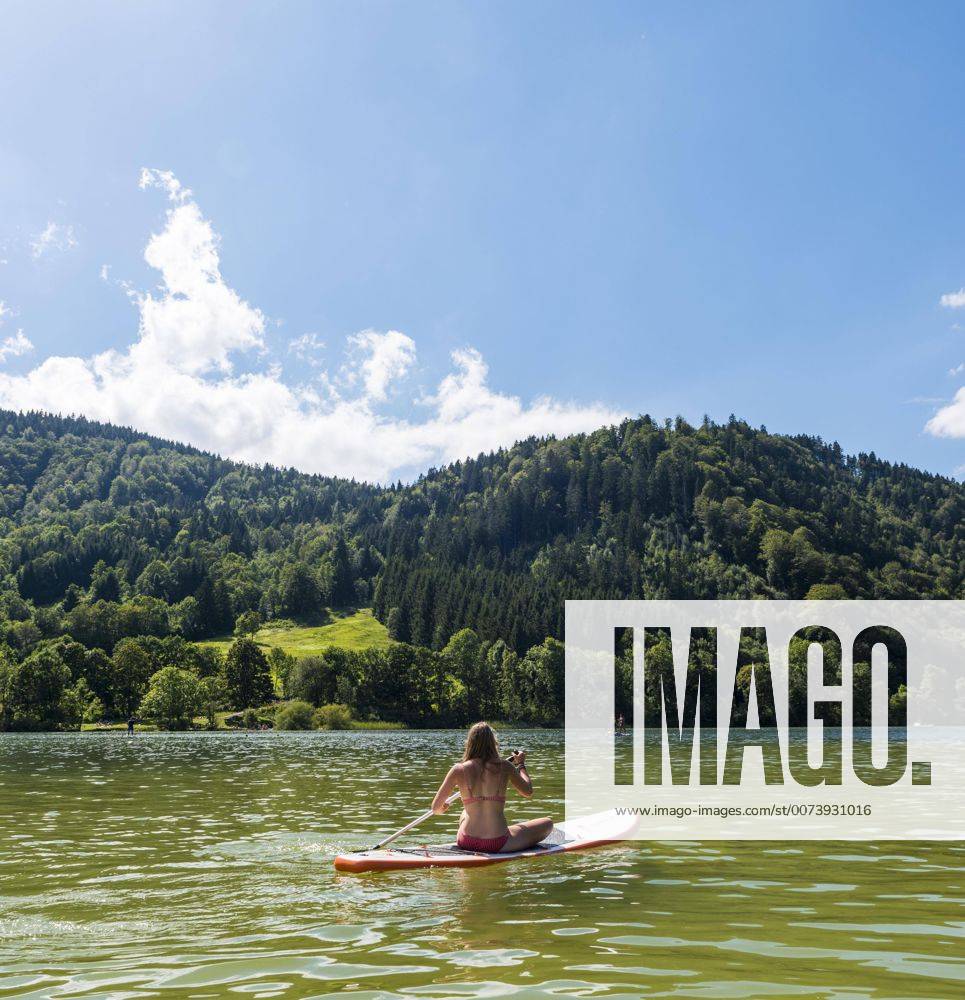 Junge Frau sitzt auf einem Stehpaddel, Stand-Up-Paddel oder SUP, Schliersee, Oberbayern, Bayern, Deutschland, Europa