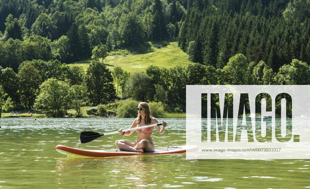 Junge Frau sitzt auf einem Stehpaddel, Stand-Up-Paddel oder SUP, Schliersee, Oberbayern, Bayern, Deutschland, Europa