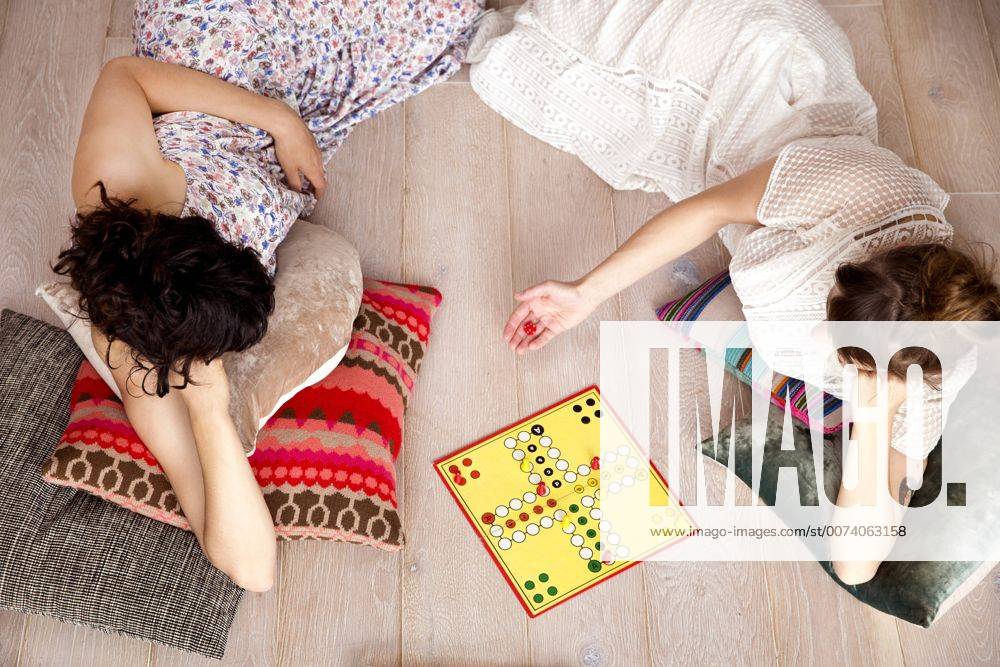 Top view of two best friends lying on the floor at home playing ludo model released Symbolfoto property released TSFF000111